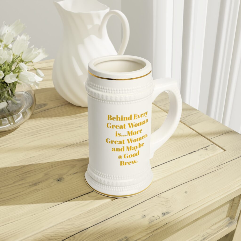 White ceramic stein mug with gold trim and "Behind every great woman is... more great women, and maybe a good brew" in gold text. Empowering women's beer mug gift.