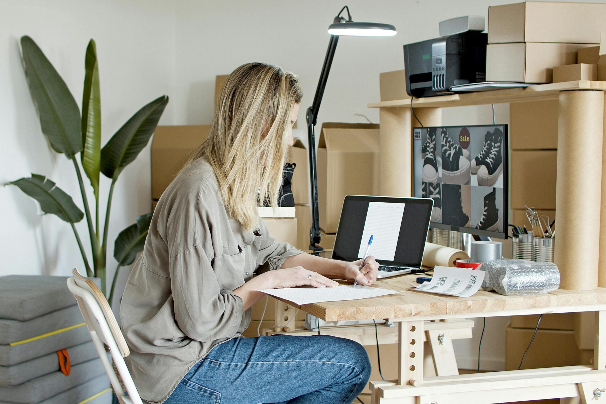 Focused woman entrepreneur working on her online passion project, efficiently managing orders and shipments from her home office, supported by digital tools including potential AI applications.