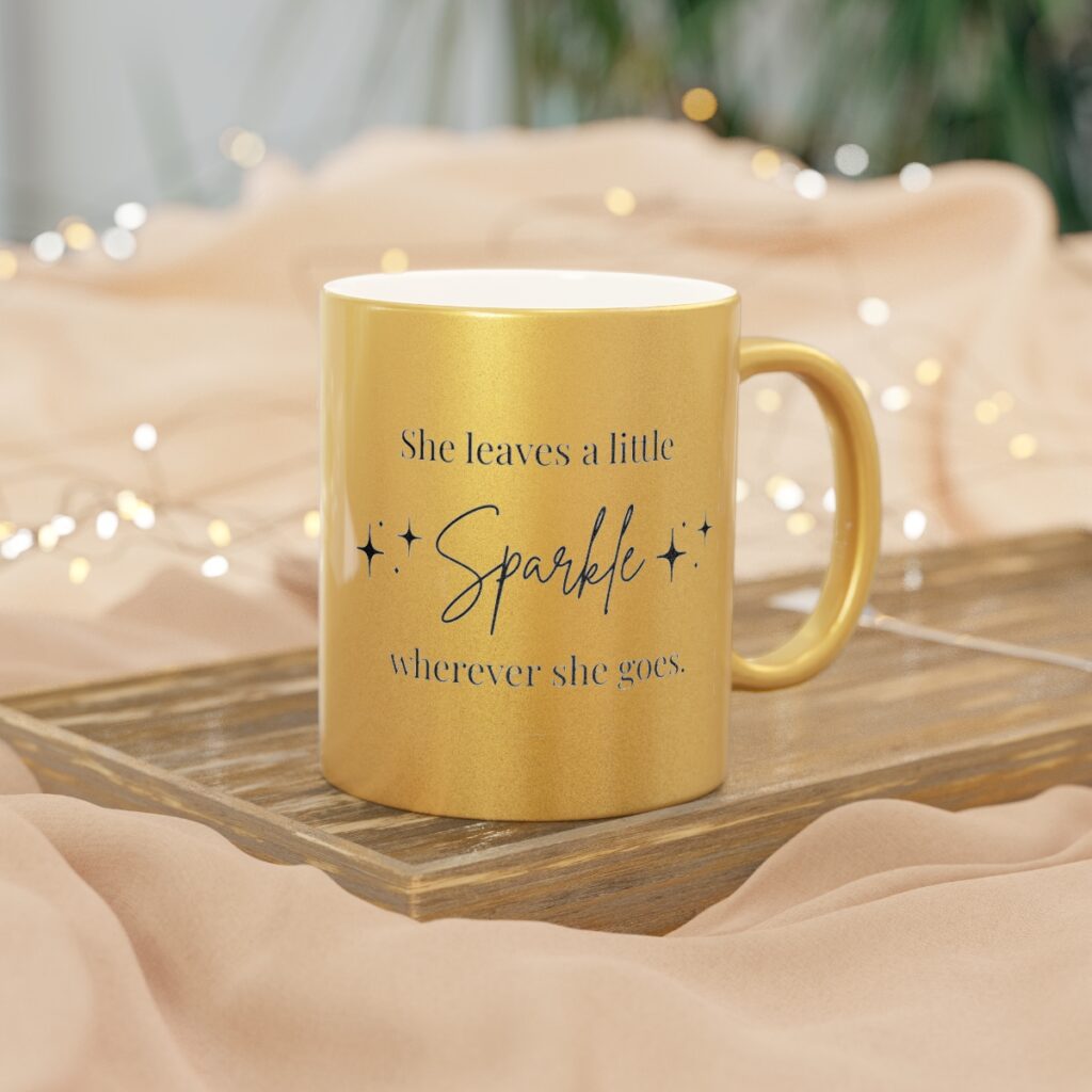 Close-up of a shimmering gold metallic coffee mug with black script text that reads: "She leaves a little sparkle โจ wherever she goes."