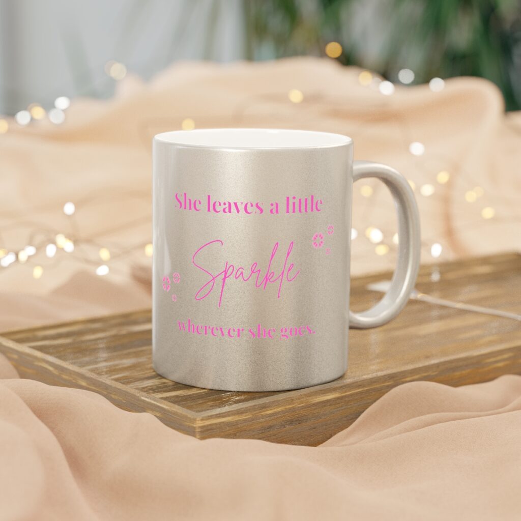 Close-up of a shimmering silver metallic coffee mug with pink script text that reads: "She leaves a little sparkle โจ wherever she goes."